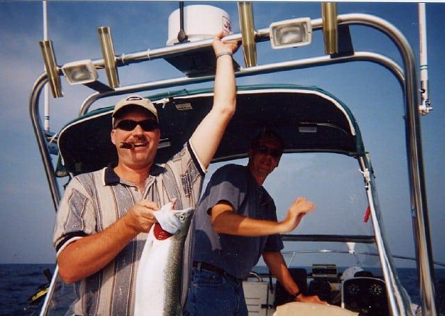 Two men on a Pro Line 201 boat, one holding a fish, with an Atlantic Towers Arch visible above.