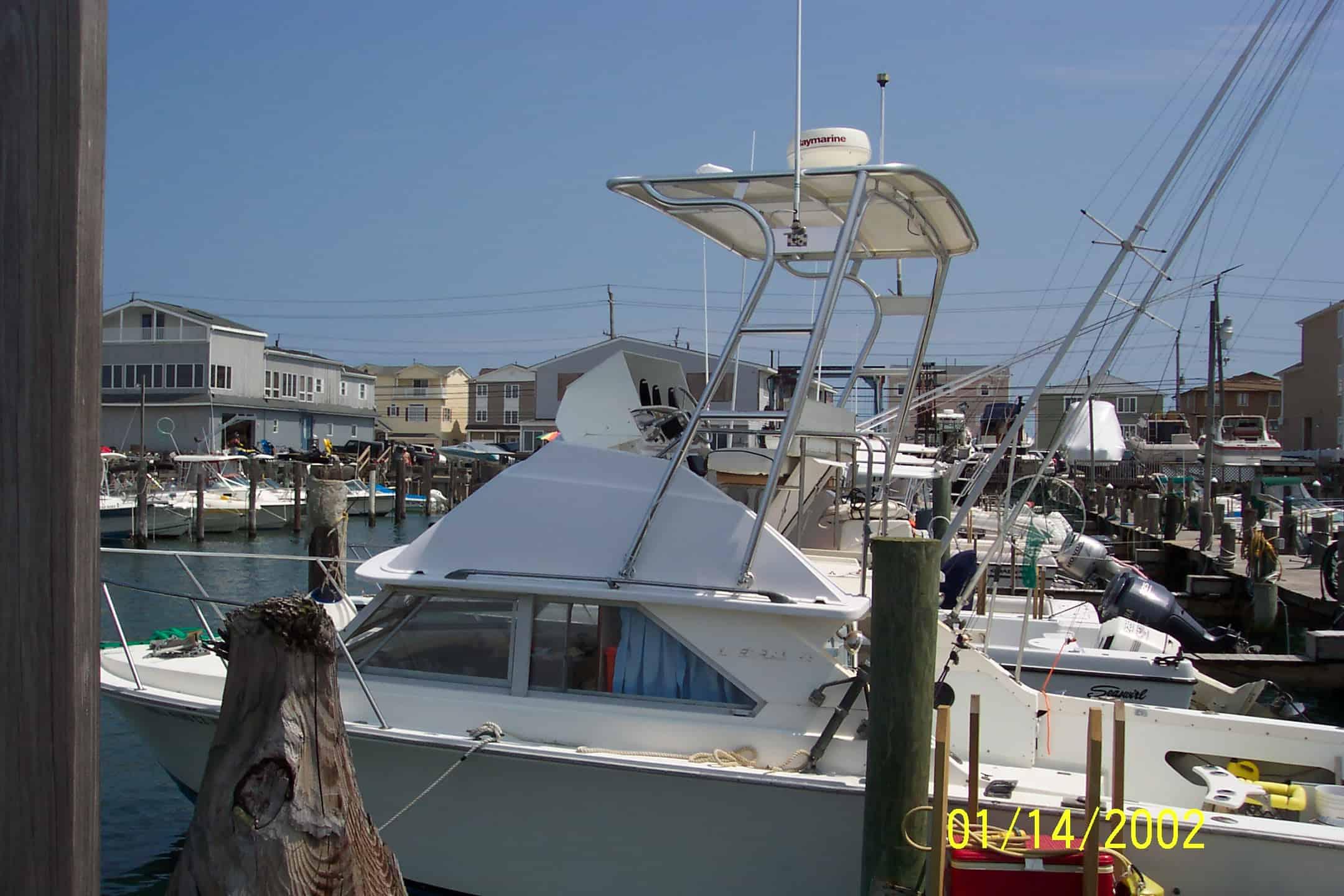 A white boat docked in a marina featuring an Atlantic Towers Arch structure. Buildings and other boats are visible in the background.