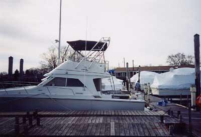 Trojan 10.8 Meter Sedan boat docked with Atlantic Towers Arch and a black canopy on top near other covered boats.