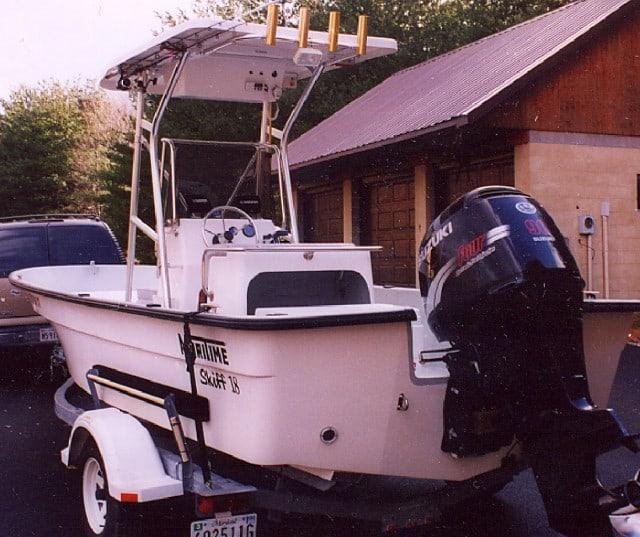 Maritime Skiff boat on trailer with installed Atlantic Towers T-Top and Suzuki outboard motor near building and vehicle.