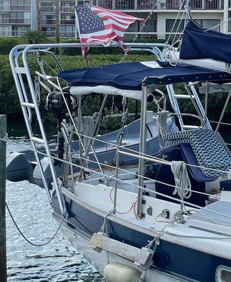 Sailboat equipped with Atlantic Towers Arch, blue canvas cover, American flag, and docked near a marina building.
