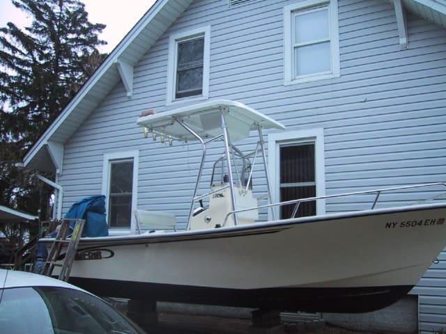 May Craft Console boat with Atlantic Towers T-Top installed, parked beside a house on supports.