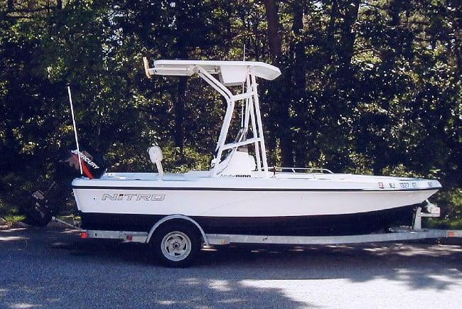 White and black Nitro 1800 boat on a trailer with an installed Atlantic Towers T-Top, parked near green trees.