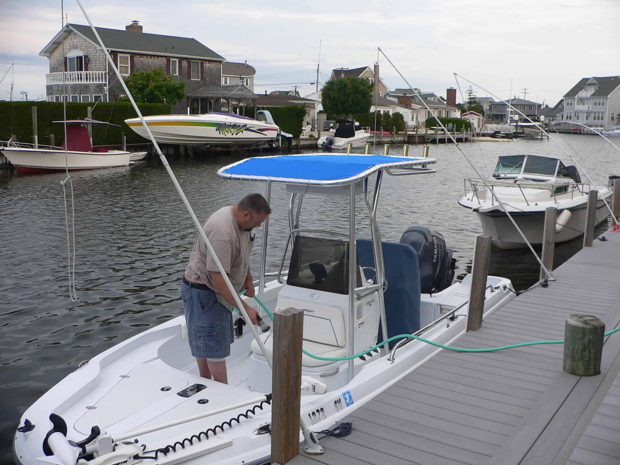 A person is installing an Atlantic Towers T-Top on a Triumph 190 Bay boat at a marina.