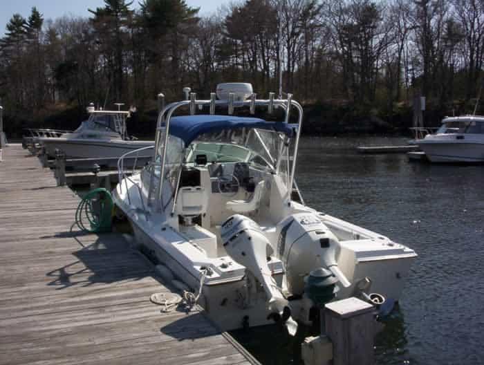 Aquasport boat docked with an installed Atlantic Towers arch and outboard motors by a wooden pier in a wooded marina.