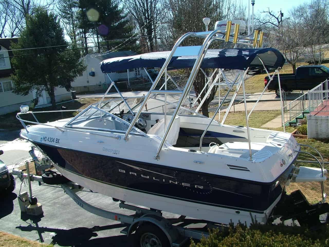 Bayliner 192 Discovery boat on trailer with installed Atlantic Towers arch and blue canvas covers in a driveway.