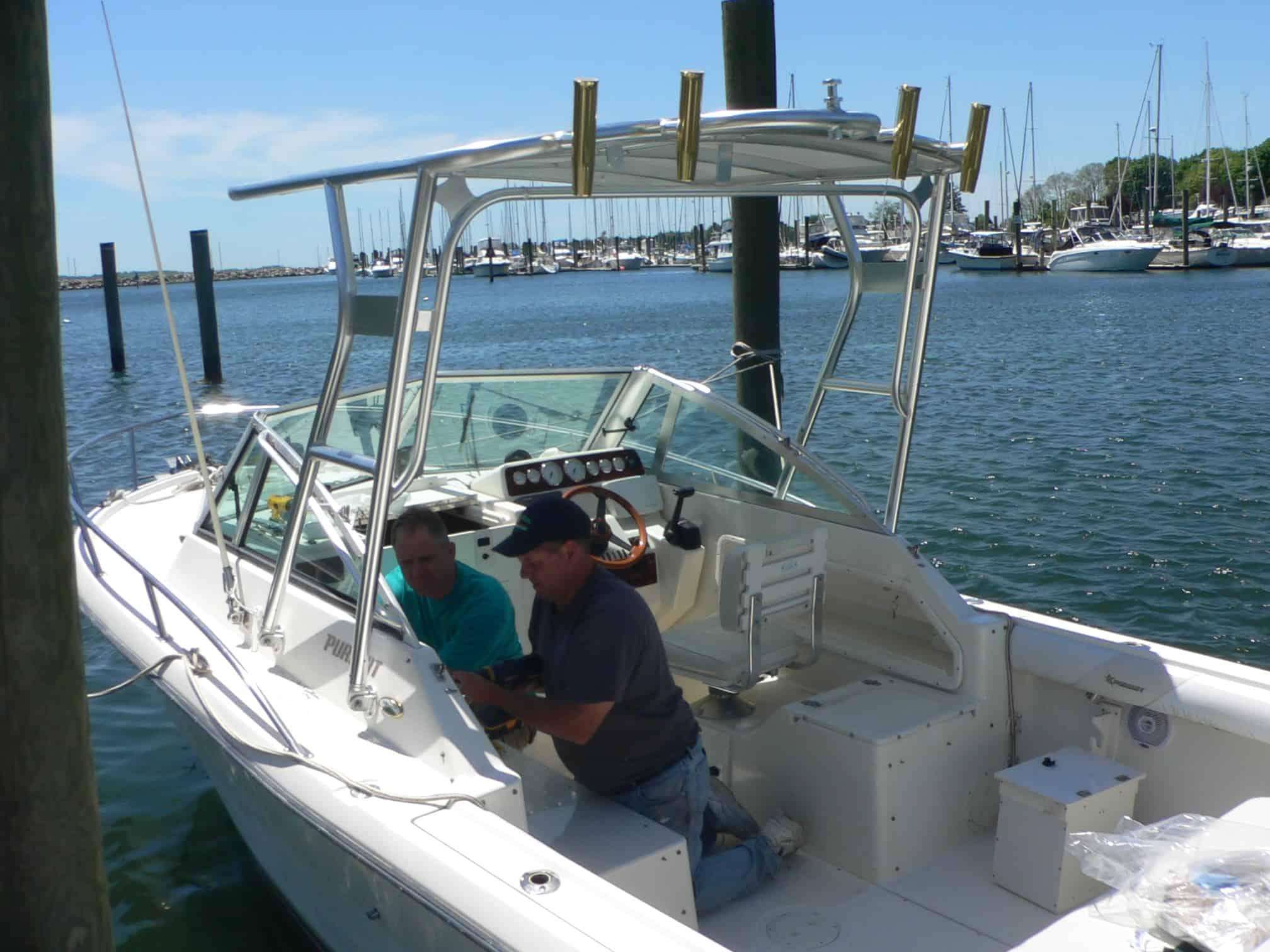 Two men working inside a Pursuit 2460 Denali boat equipped with an Atlantic Towers Top with mounted rod holders at a dock.