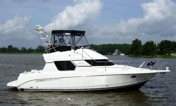 Silverton 350 Convertible boat with installed Atlantic Towers Arch cruising on calm water near a grassy shoreline.