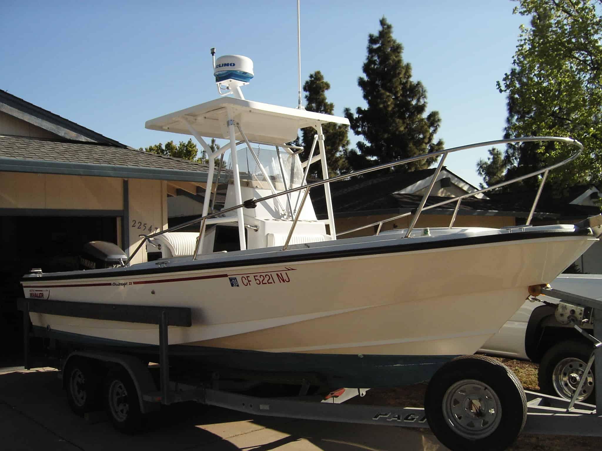 Boston Whaler Outrage boat with installed Atlantic Towers T-Top on trailer parked in driveway near house and trees.