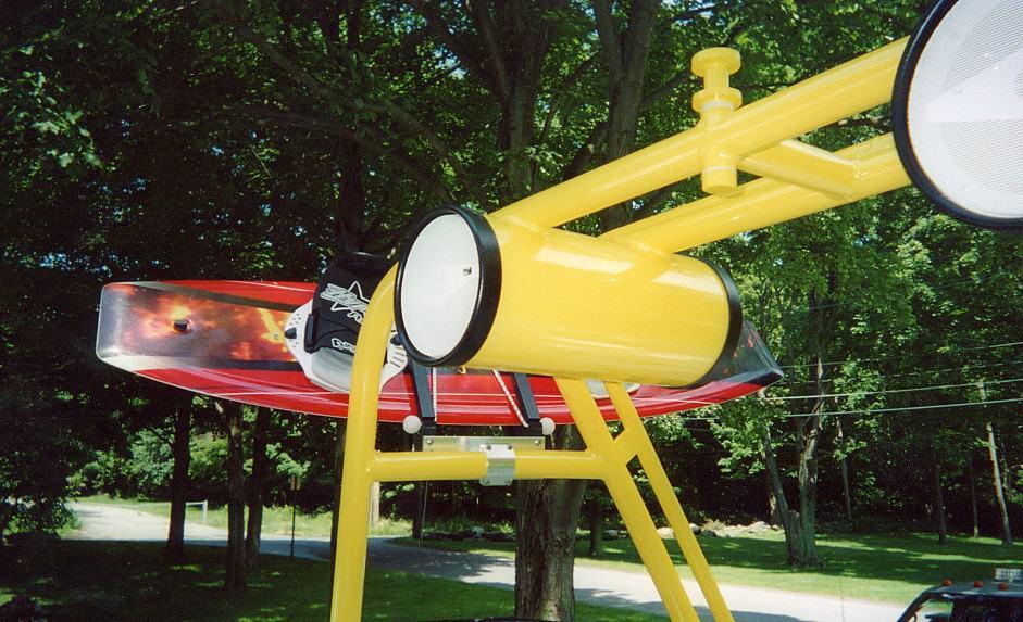 Atlantic Towers Air Tower with yellow frame holding a red and black wakeboard against a background of green trees and grass.