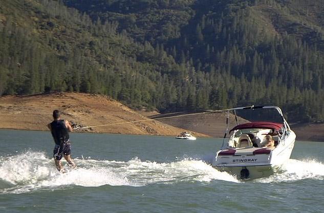 A person water skiing behind a Stingray 220LX boat equipped with an Atlantic Towers Air Tower on a lake.