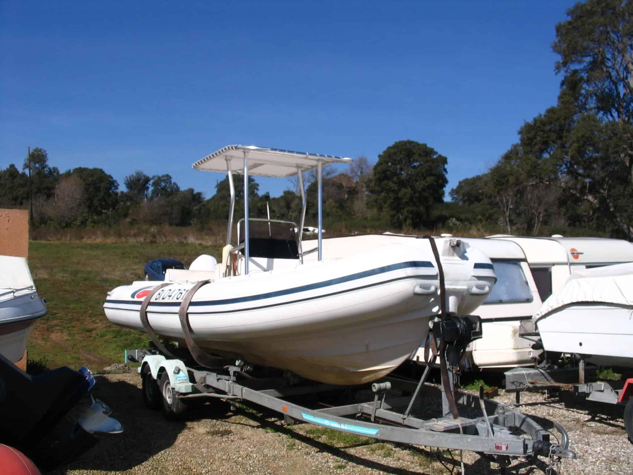 Selva RIB boat on trailer with Atlantic Towers T-Top installed, parked on gravel near other boats and trees.