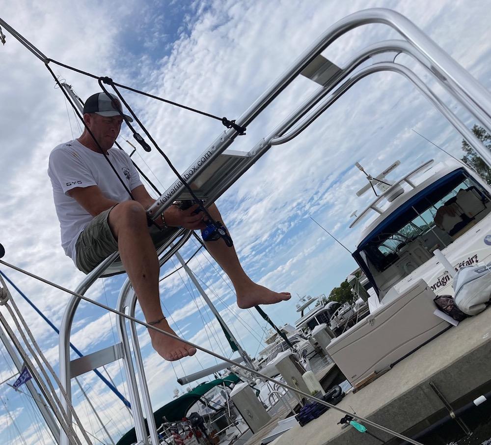 A person sits on an Atlantic Towers Arch framework at a marina, holding equipment with boats in the background.