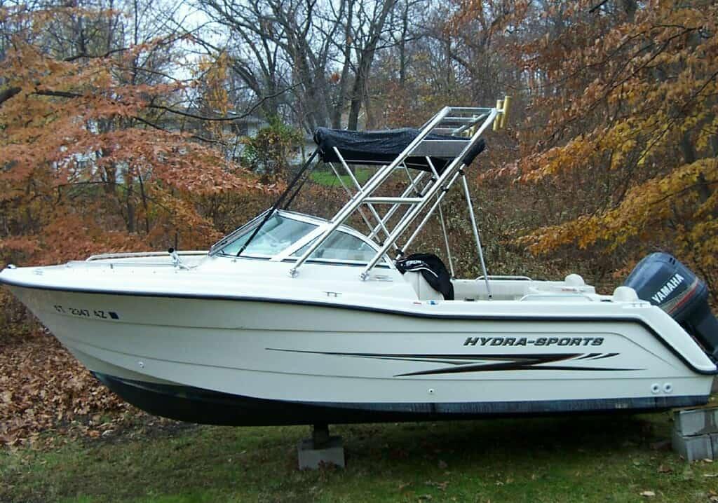 Side view of a Hydra Sports 202 Dual Console boat with an installed Atlantic Towers Arch, resting on blocks near autumn trees.
