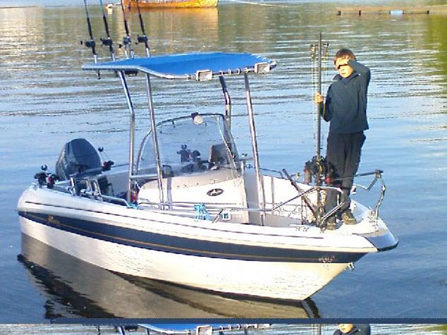 Yamarin 56CC boat with installed Atlantic Towers T-Top and a person standing near the bow holding fishing rods on calm water.