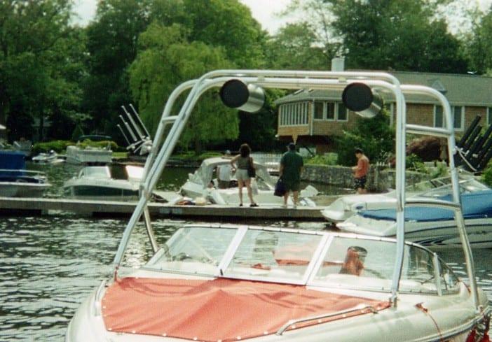 Front view of a Stingray 220 boat with an installed Atlantic Towers Air Tower, docked near a pier with people and houses in the background.