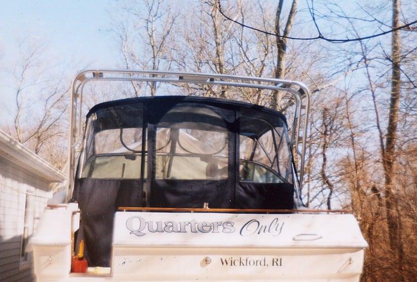 Rear view of a Sea Ray 300 Weekender boat with a black enclosure and an installed Atlantic Towers arch, docked near trees.