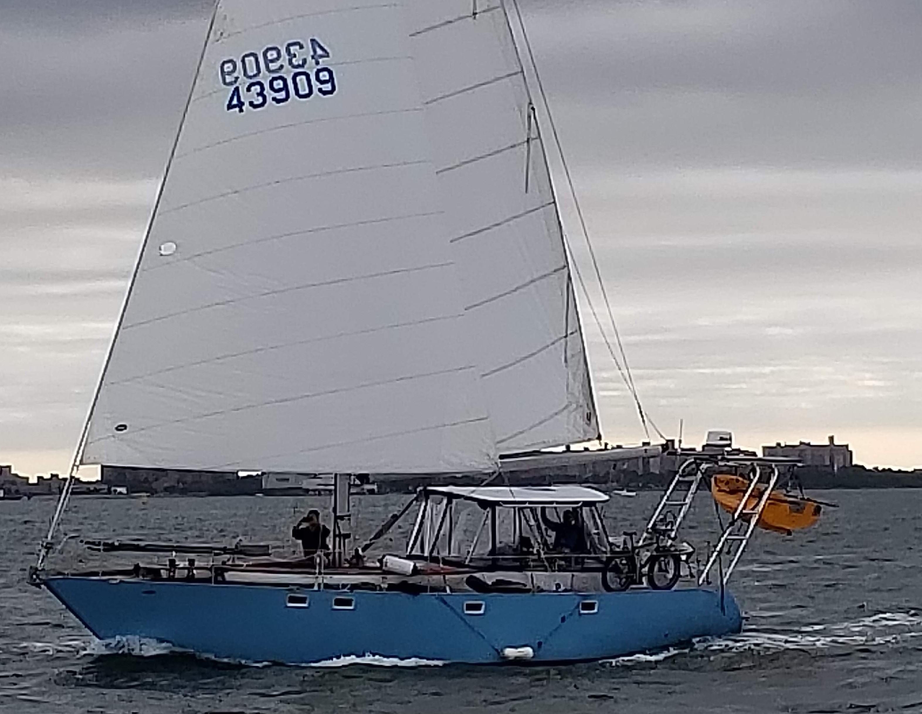 Sailing yacht with Atlantic Towers Top, featuring a blue hull and kayak mounted on the stern, navigating a gray sea.
