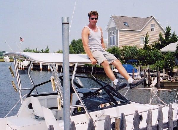 Man sitting on the stainless steel Atlantic Towers Top mounted on the Bayliner 2509 Trophy Walkaround boat docked near a house.