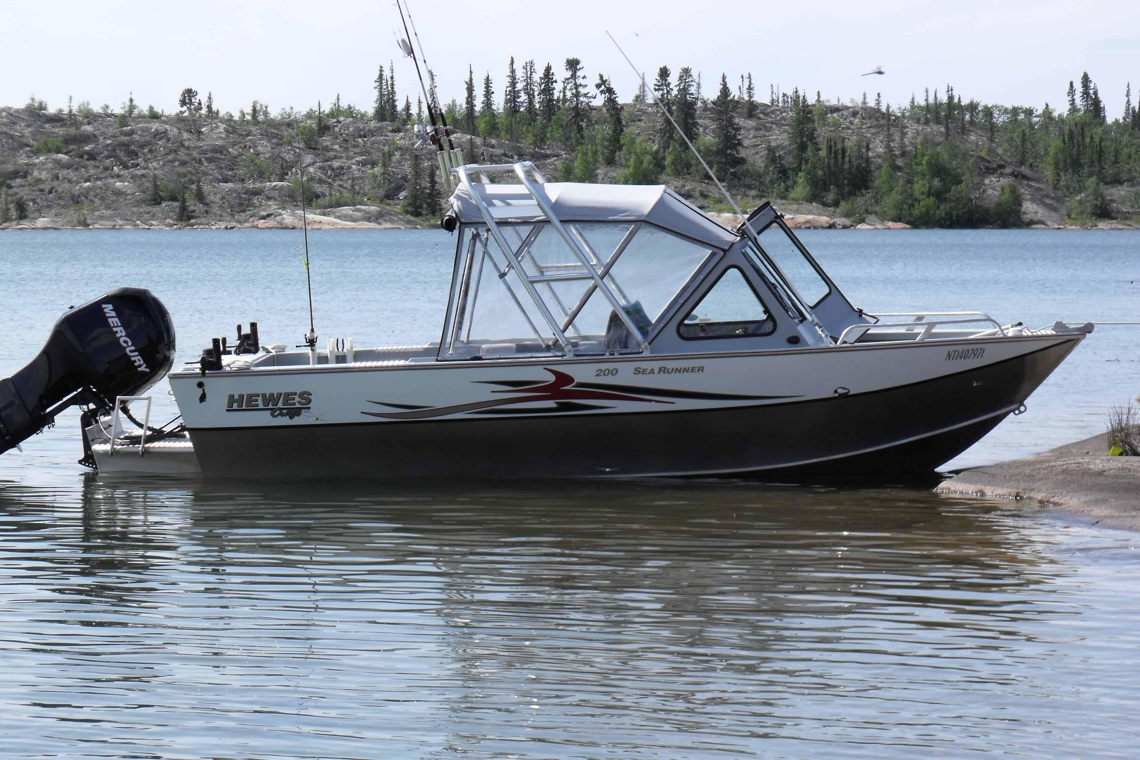 Hewes 200 Sea Runner boat with Atlantic Towers Arch installed, floating near a rocky shoreline with trees in the background.